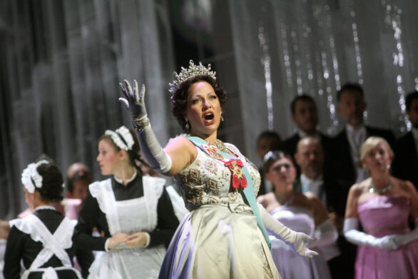 Degli attori sono in scena sul palco durante l'opera "Elisabetta Regina d'Inghilterra". La regina ,in primo piano, sta cantando. Sullo sfondo altri personaggi.