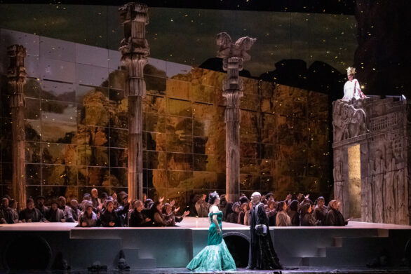 Scena dell'opera "Turandot". Un'uomo con un mantello nero sta guardando una donna vestita di verde. Altri attori intorno a loro cantano